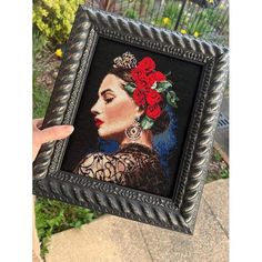 a woman's hand holding up a framed painting with red roses in her hair