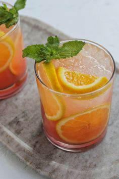 two glasses filled with water and fruit on top of a table next to a pitcher