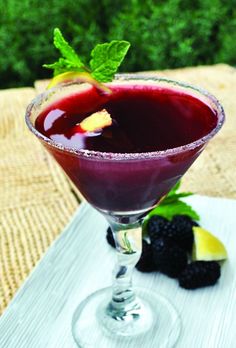 a close up of a drink in a glass on a table with berries and mint