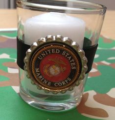 a candle that is sitting in a glass cup with a marine seal emblem on it