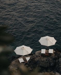 three white umbrellas sitting on top of a rock next to the ocean in front of some chairs