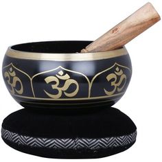 a black and gold singing bowl with a wooden stick sticking out of it