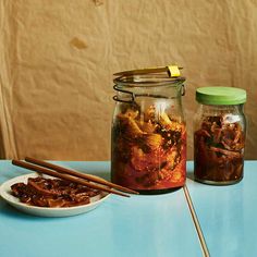 two jars filled with food sitting on top of a table next to chopsticks