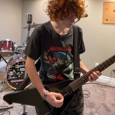 a young man with red hair playing an electric guitar in front of a drum set