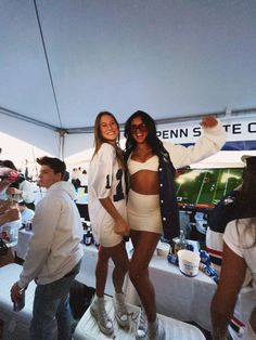 two women standing next to each other in front of a tent at a sporting event