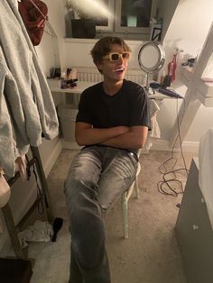 a young man sitting in a chair with his arms crossed, wearing sunglasses and looking at the camera