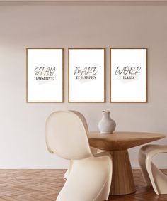 three posters on the wall above a table with two chairs and a vase in front of it