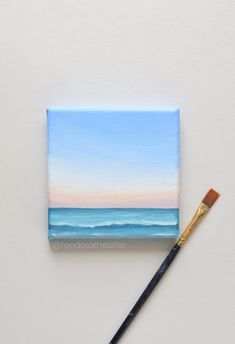 an acrylic painting of the ocean with a paintbrush next to it on a white surface