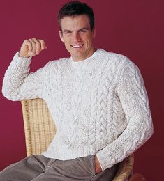 a man sitting in a wicker chair wearing a white cabled sweater and khaki pants