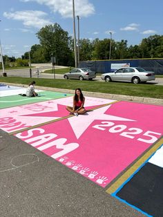 a woman sitting on the ground in front of a large pink star painted parking lot