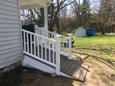 a porch with white railings next to a house in the background and trash cans on the ground