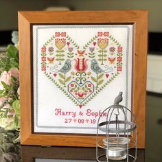 a cross - stitch heart with two birds on it and a birdcage next to it