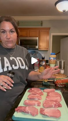 a woman standing in front of a counter with raw meat on it, and cooking