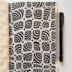 an open notebook with black and white designs on it, next to a fountain pen