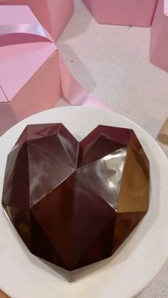 a heart shaped chocolate sitting on top of a white plate next to pink and gold boxes