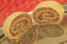 two cinnamon rolls are on a silver plate with red table cloth behind them and one is cut in half to show the inside