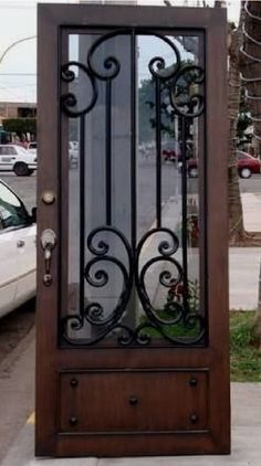 a wooden door with wrought iron design on the side walk next to a white car