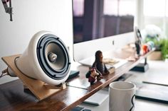 a speaker sitting on top of a wooden desk next to a cup and figurine