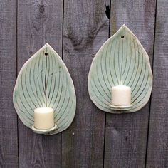 two tea light holders made out of leaves on a wooden fence with a candle in the center