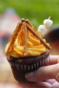 a hand holding a chocolate cupcake with orange frosting and cinnamon sticks on top