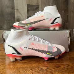 a pair of white and pink soccer cleats sitting on top of a wooden floor