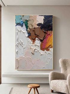 an abstract painting hangs on the wall next to a chair and footstool in a living room