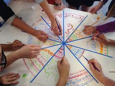 a group of people sitting around a table drawing on paper