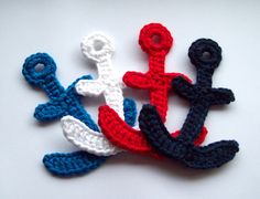 three crocheted anchors on a white surface with blue, red and white yarn