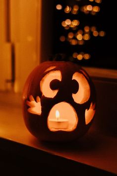 a carved pumpkin sitting on top of a window sill with a lit candle in it