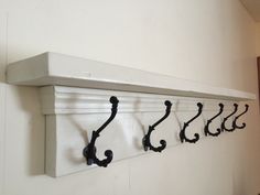 the coat rack has five hooks on it and is mounted to the wall with wrought iron brackets