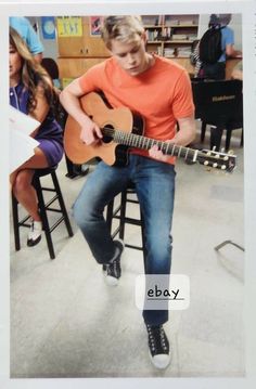 a young man sitting on top of a stool holding an acoustic guitar in front of him