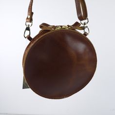 Embossed Leather Shoulder Round Bag Handmade Cross Body Saddle Vintage Handbag Height: 6.9 inches (15.5 cm) Width: 6.9 inches (15.5 cm) Depth: 1.4 inches (3.5 cm) Strap Length: max 56 inches (143 cm) This is a Handmade Cross-body Bag in Brown, Natural Tan and Black color. It has one compartment and secures with a zipper. The strap is removable and adjustable for your shoulder. Natural vegetable tanned leather will age and darken with the sun just like your own skin. Sun exposure and daily handli Brown Satchel With Removable Pouch And Round Handle, Brown Shoulder Bag With Adjustable Strap And Round Handle, Brown Saddle Shoulder Bag With Brass Hardware, Vintage Brown Saddle Bag With Detachable Strap, Round Leather Shoulder Bag For Everyday Use, Brown Round Bag For Daily Use, Brown Round Case Shoulder Bag For Travel, Handmade Saddle Shoulder Bag For Travel, Brown Crossbody Shoulder Bag With Coin Pocket