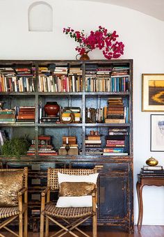 two chairs in front of a bookshelf filled with books and vase full of flowers