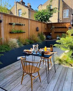 an outdoor dining area with wooden decking and table set for two, surrounded by greenery