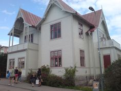 several people are walking in front of a large white house with red roof and windows