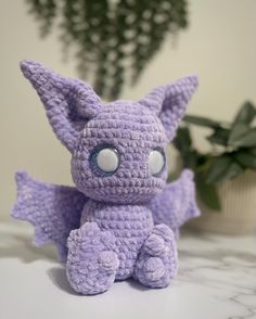 a purple crocheted stuffed animal sitting on top of a table next to a potted plant