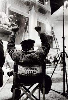 a man sitting in a chair with his arms up while holding a sign that reads federico fellin