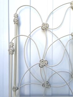 a white metal headboard with ornate designs on the top, and bottom part of it's frame