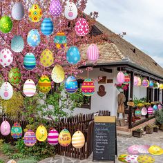 an assortment of colorful easter eggs hanging from a tree in front of a small building