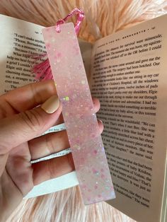 a person holding an open book with pink glitters on it and a string attached to the bookmark