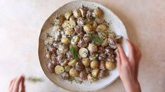 two hands reaching for a plate of food with potatoes and herbs on it, while another person holds out their hand to the plate