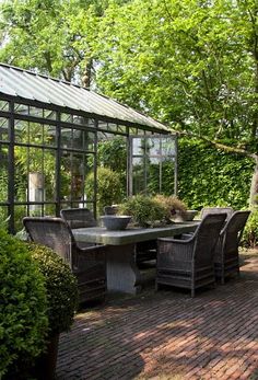 a table and chairs in the middle of a brick patio with a glass house behind it