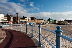 a boardwalk on the beach with buildings in the background and blue skies above it,