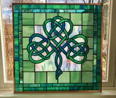 a stained glass window with a green and blue design on it's side, in front of a window sill