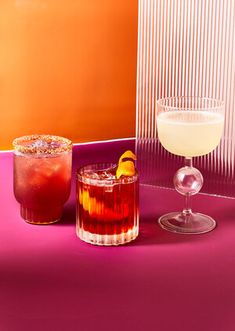 two cocktails sitting next to each other on a purple counter top in front of an orange wall