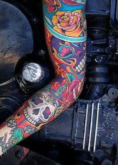 a man with tattoos on his arm and leg sitting next to a motorcycle engine compartment