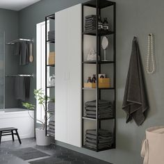 a white bathroom with black shelving and towels on the shelves, along with a potted plant