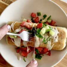 a person holding a fork and knife in a bowl with food on top of it