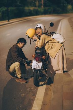 a man kneeling down next to a motorcycle on the side of a road with a helmet on his head