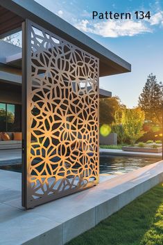 an outdoor area with grass and water in the foreground, there is a large laser cut out design on the wall